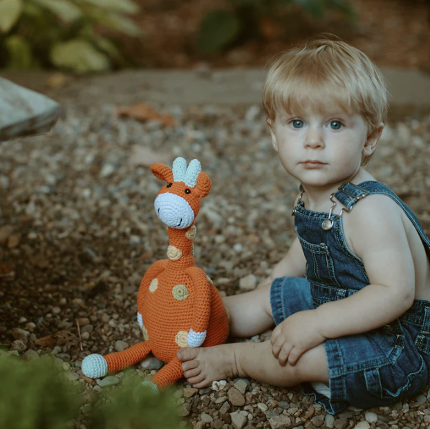 Child sitting on the ground with a crochet giraffe toy