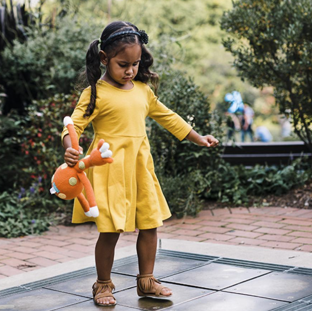 Young girl in a yellow dress holding a stuffed animal in an outdoor setting