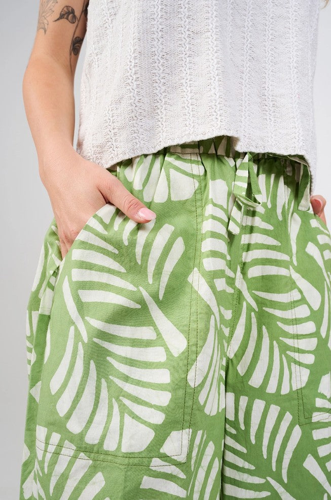 Close up photo of a hand resting inside the pocket of a pair of green pants with white leaf pattern.