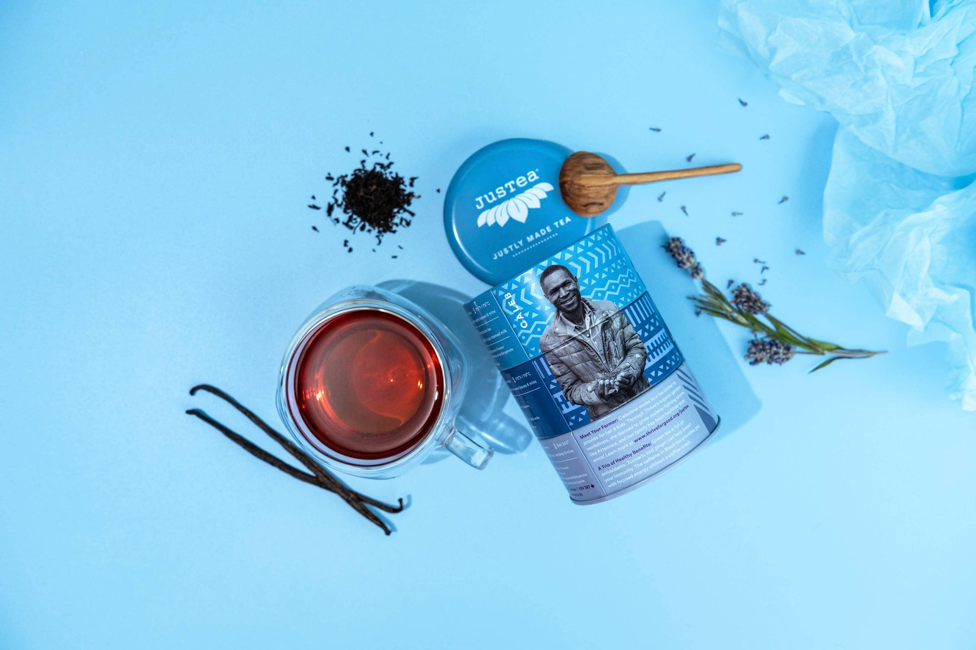 Tea canister with a lid, a cup of tea, and tea leaves on a blue background
