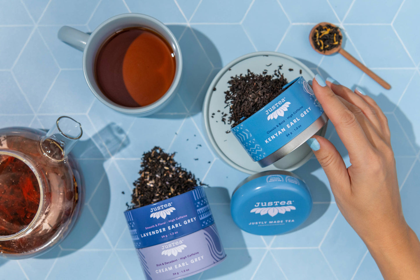 Just Tea tins with tea leaves and a cup of tea on a blue tiled surface