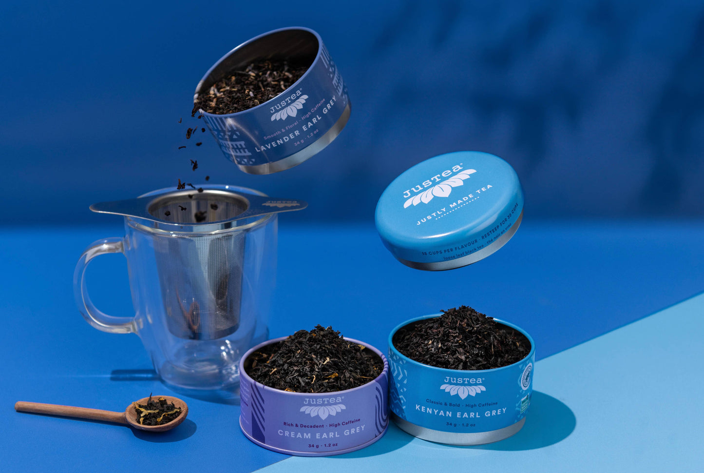 Tea-making setup with a stacking tea tins container separated to show the three different tea varieties, tea infuser, and loose tea on a blue background.