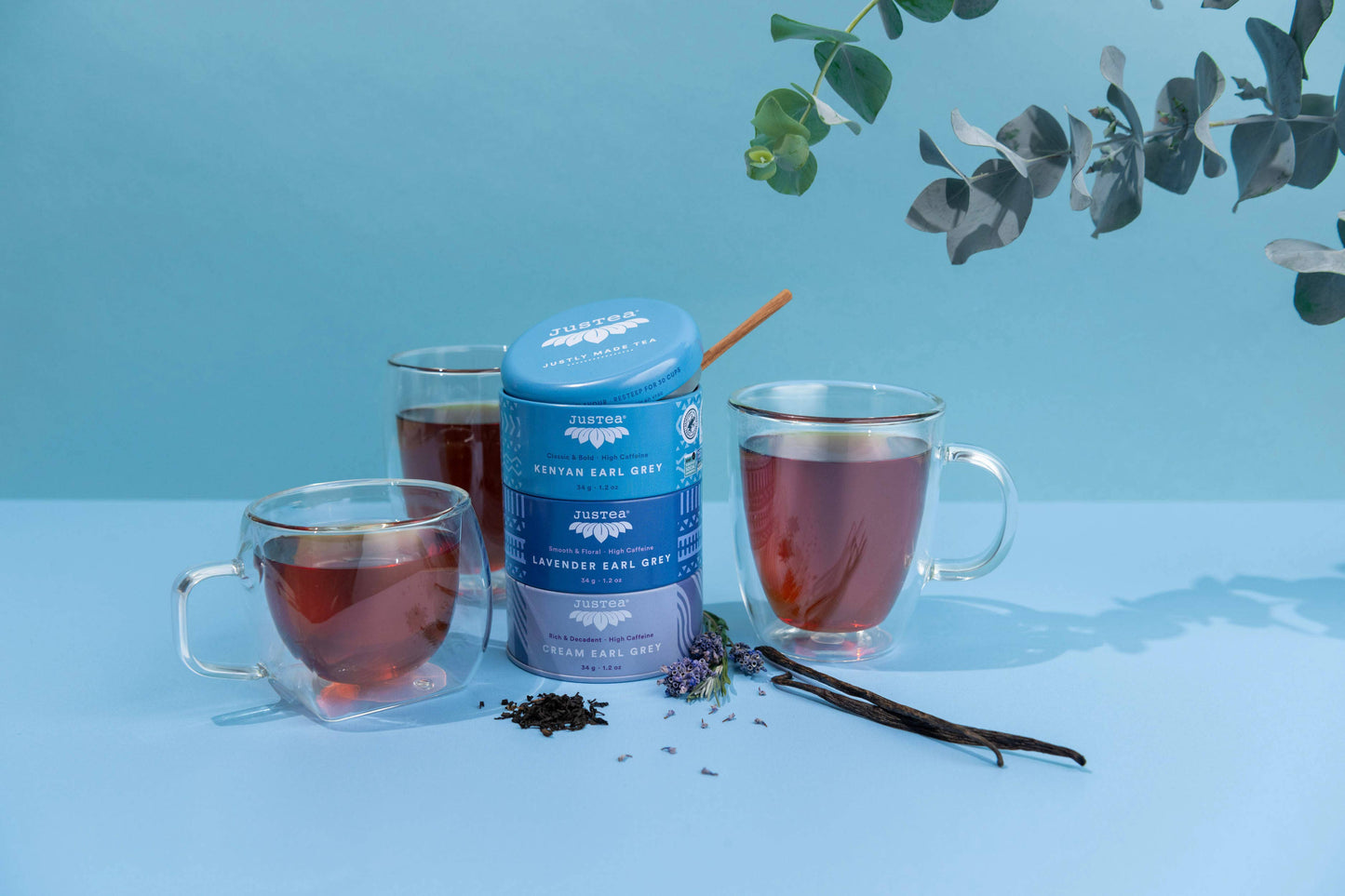 Tea canister with three glass cups of tea on a light blue background