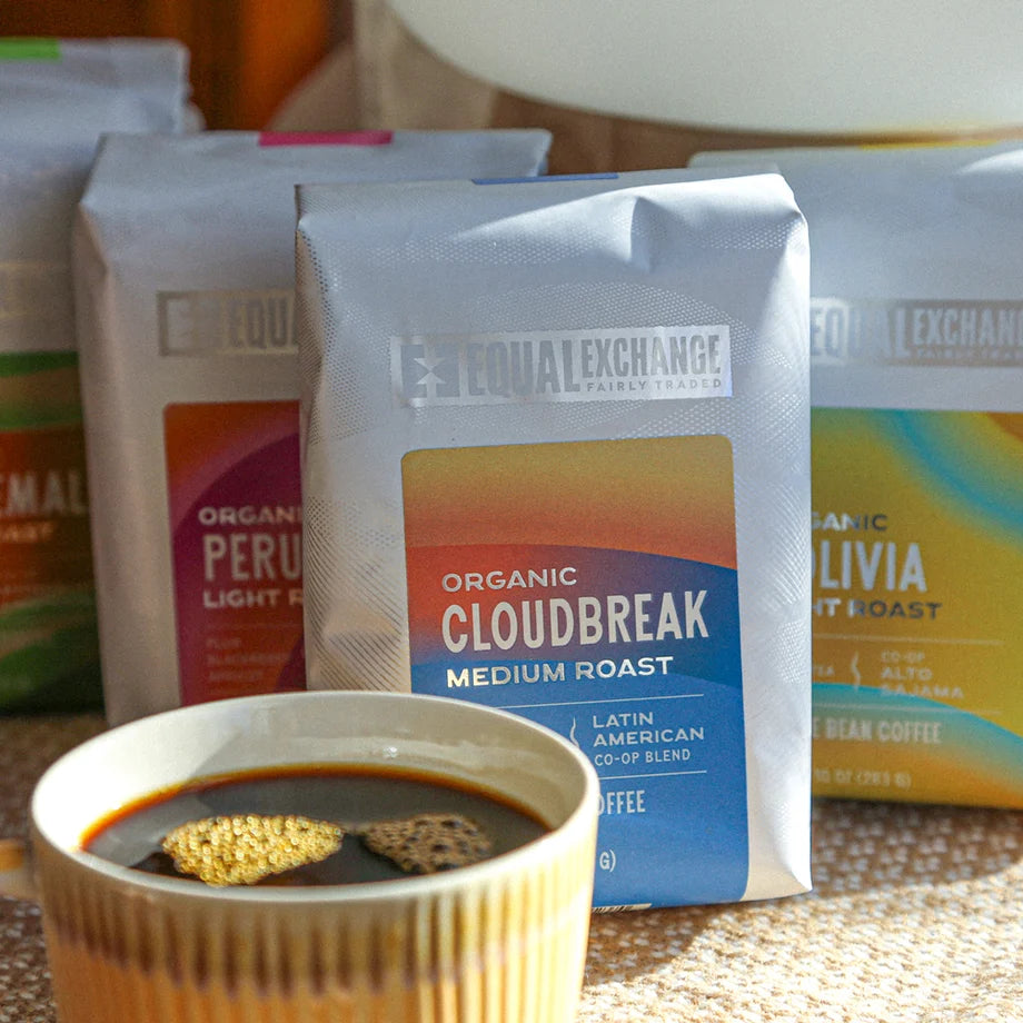 Assortment of coffee packages featuring the Cloudbreak flavor in the front, cup of brewed coffee on a burlap sack.