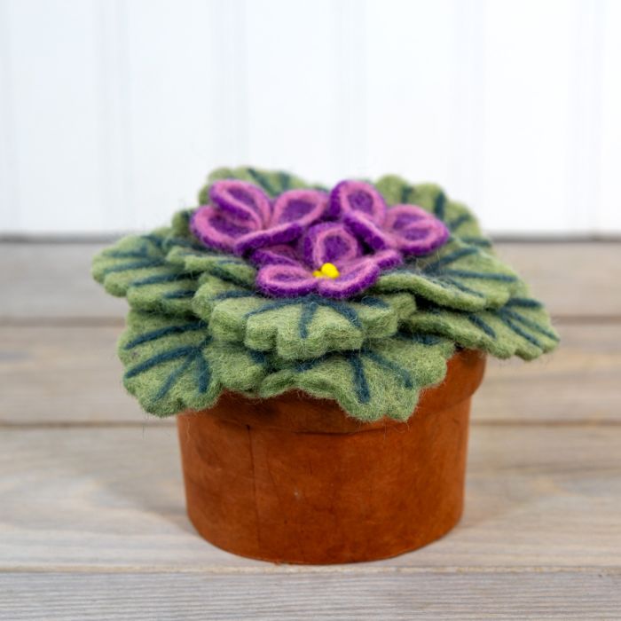 Felted flower pot with purple flowers and green leaves on a wooden surface.