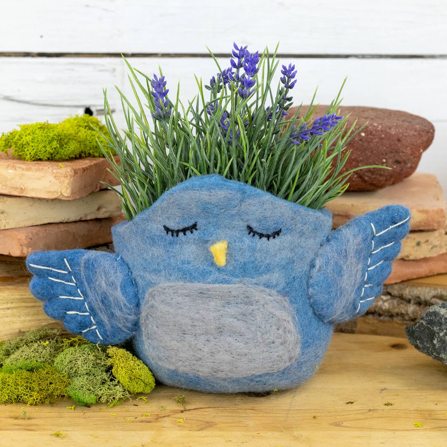 Blue bird-shaped planter with lavender and greenery on a wooden surface.