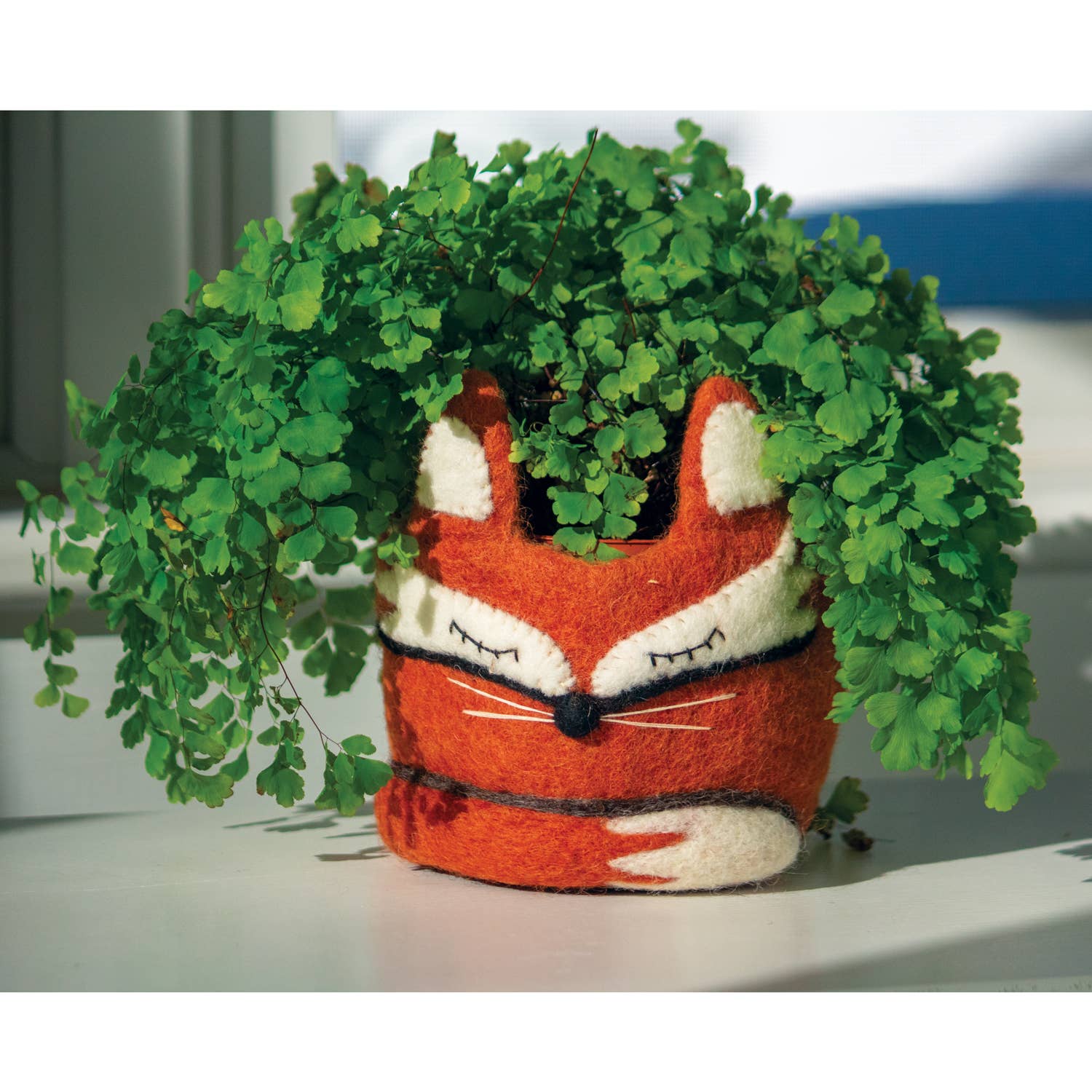 Felt fox planter with green leaves on a white surface