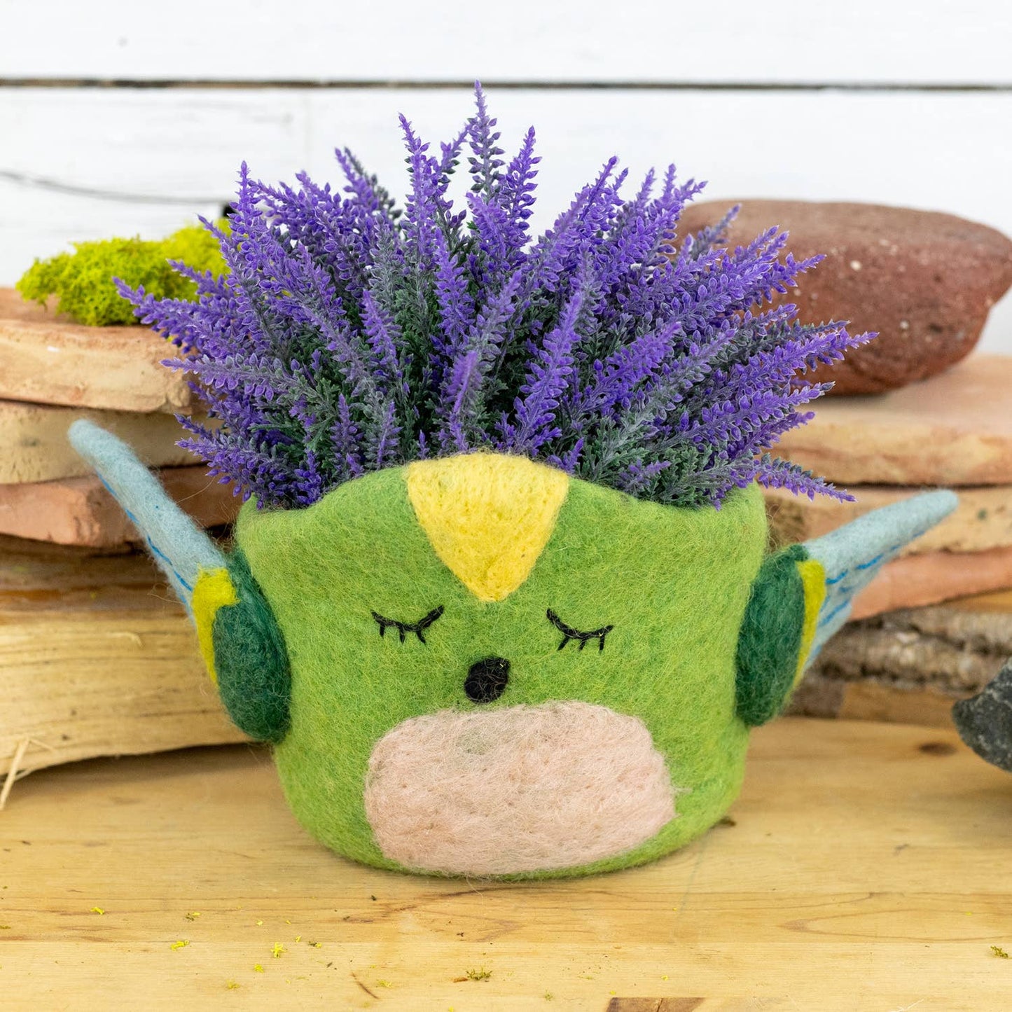 Green hummingbird pot with a face and purple flowers on a wooden surface