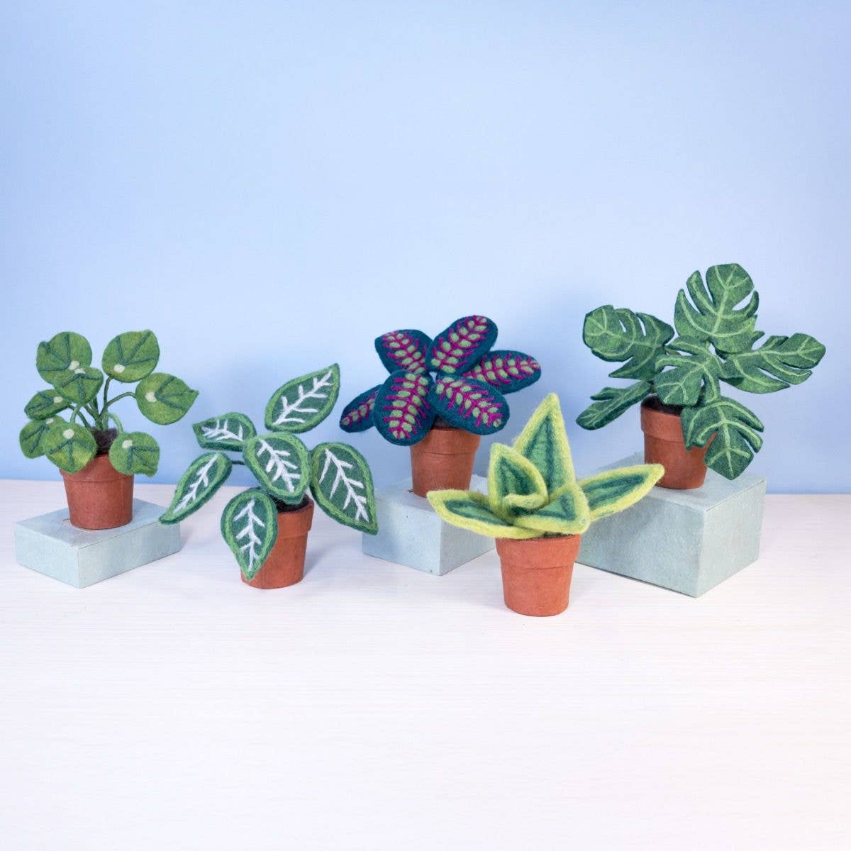 Set of felt plants in pots on a white surface with a light blue background