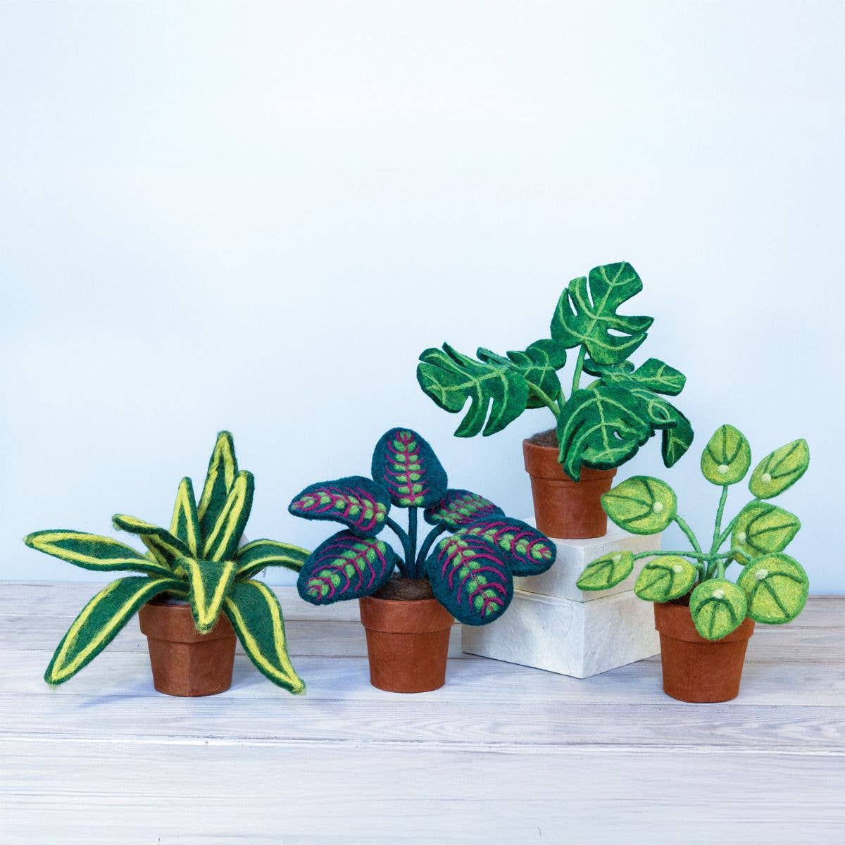 Set of felt plants in terracotta-colored paper pots on a light wooden surface with a white background