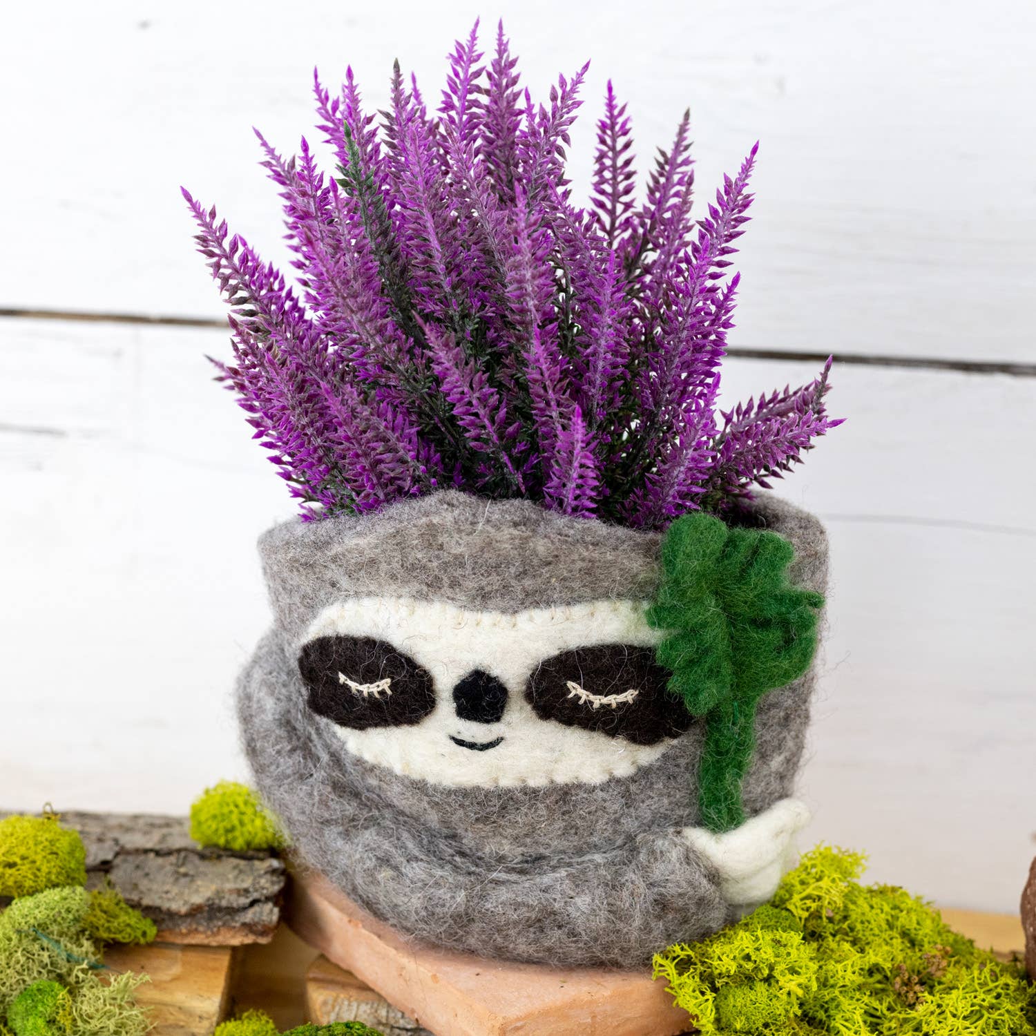 Sloth-shaped planter with purple flowers on a wooden surface