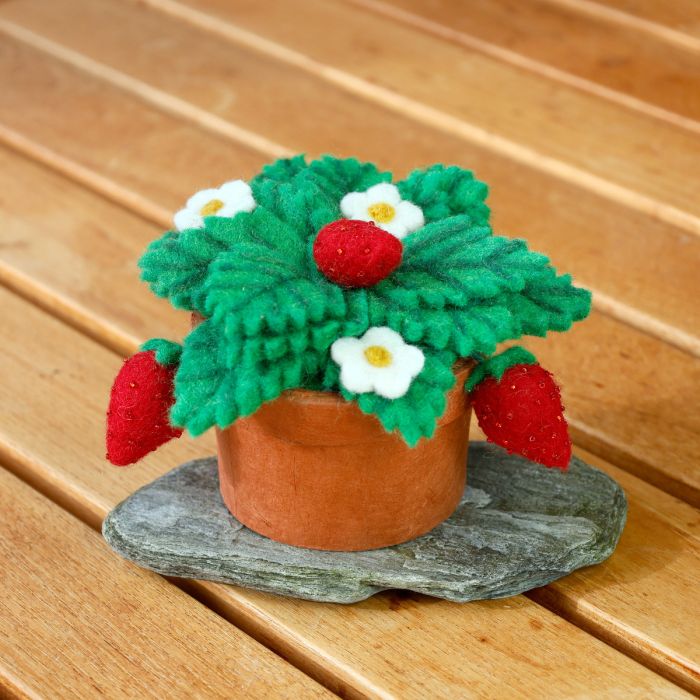 Felted potted plant with red berries and white flowers on a wooden surface