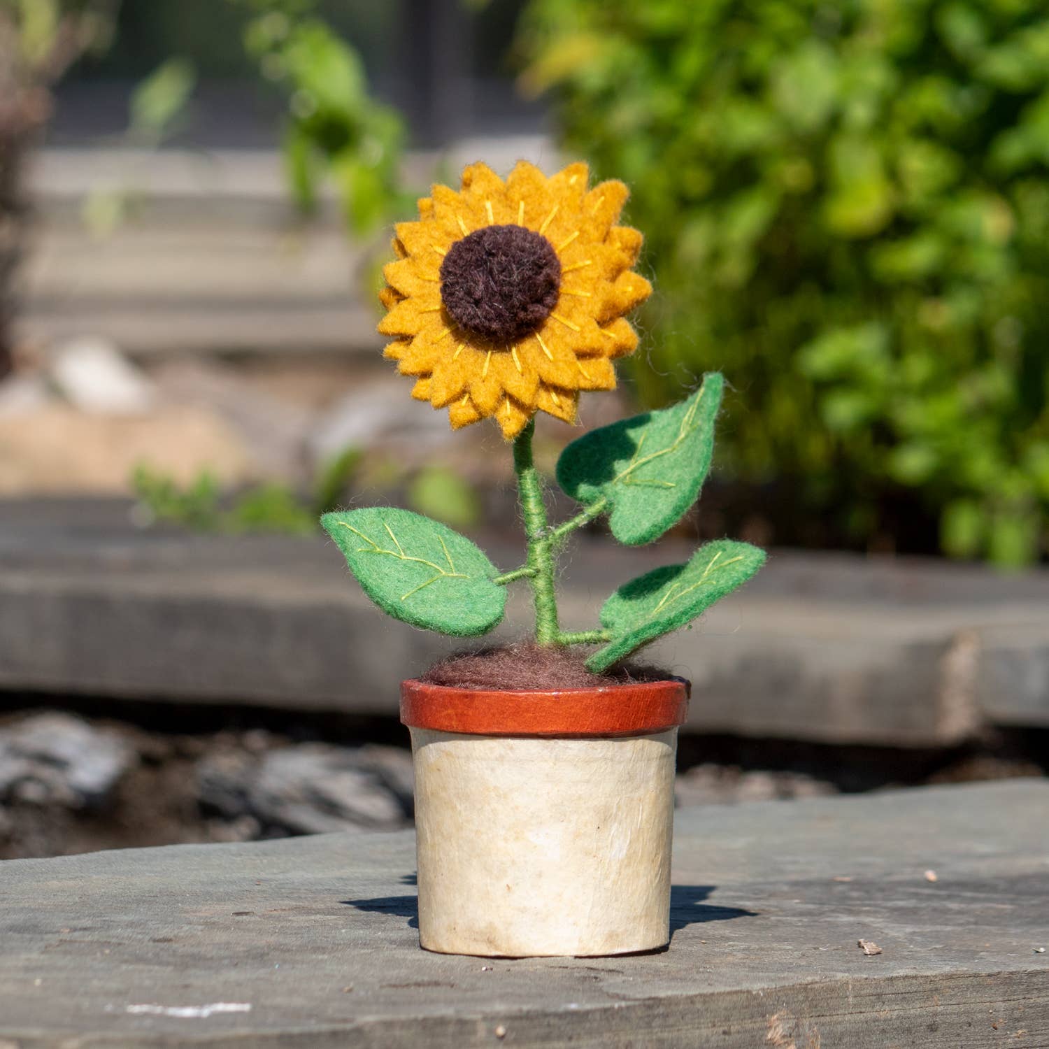 Felt sunflower in a pot on a wooden surface with a blurred natural background