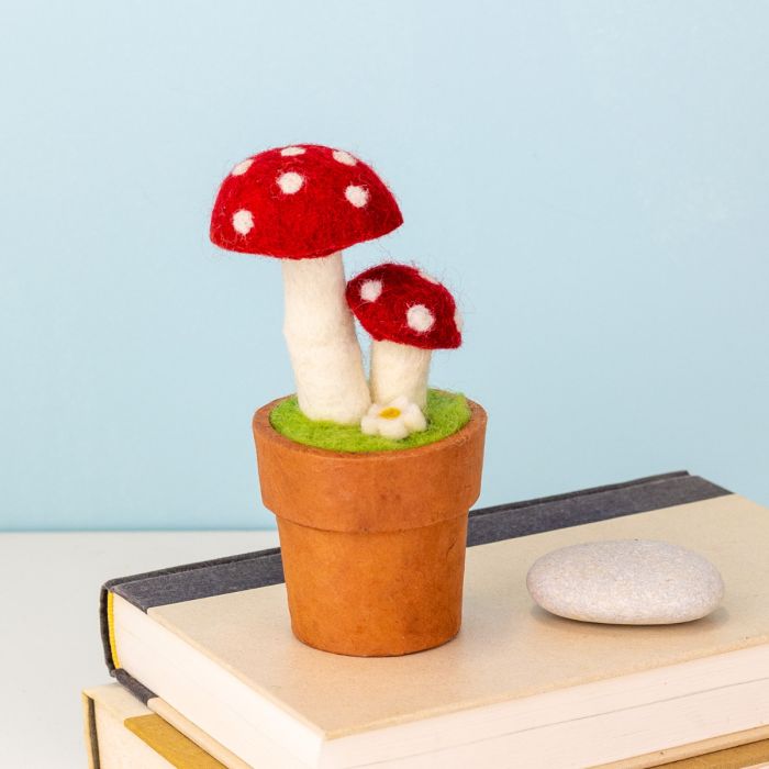 Felted red and white mushrooms in a terracotta-colored pot on a light blue background
