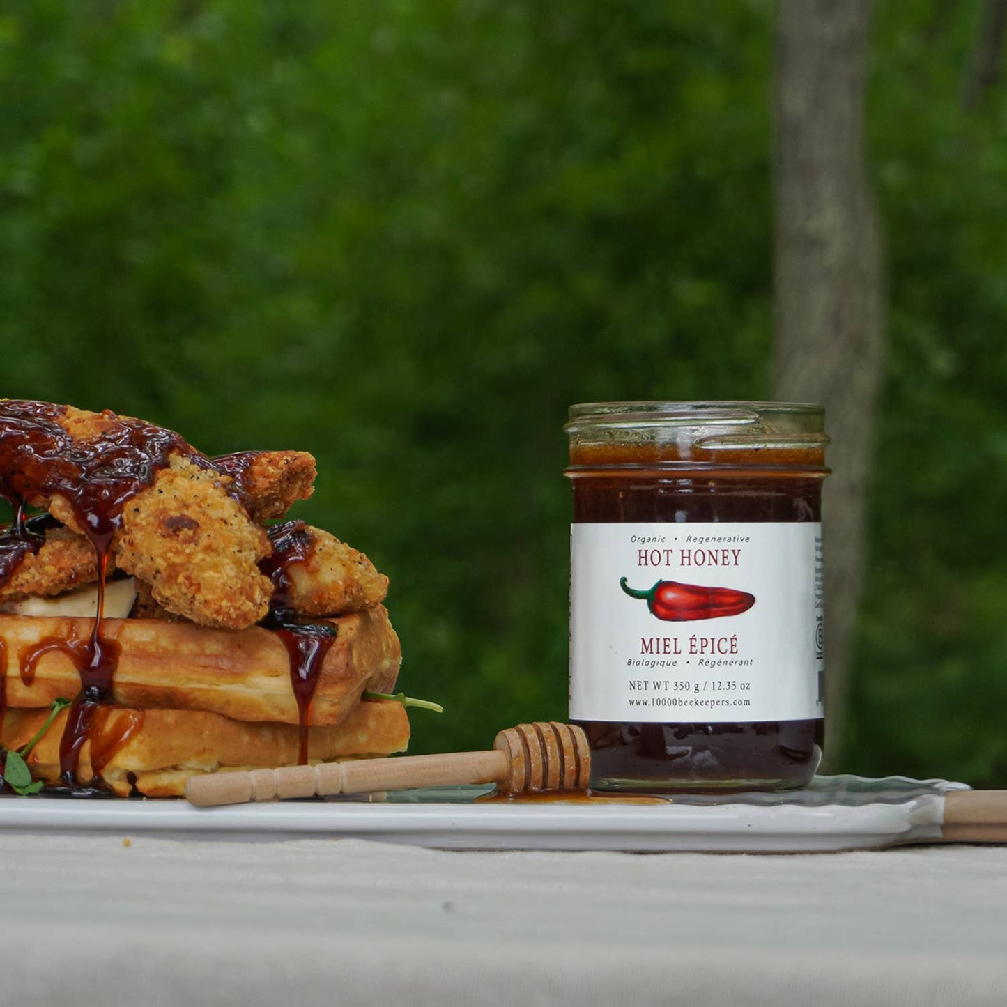 Stack of waffles with fried chicken and hot honey on a plate next to a jar of hot honey.