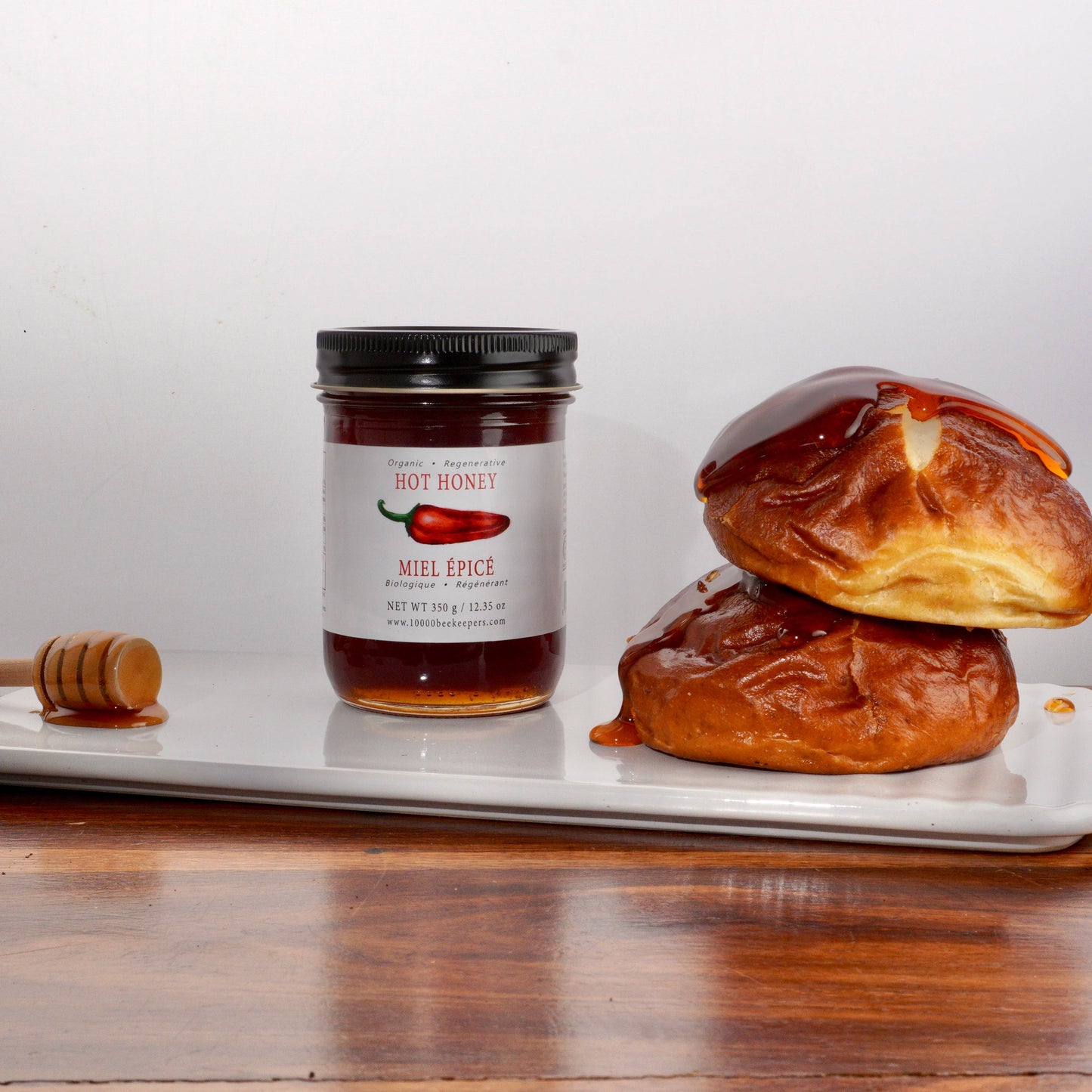 Jar of hot honey with a honey dipper and pastries on a white plate.