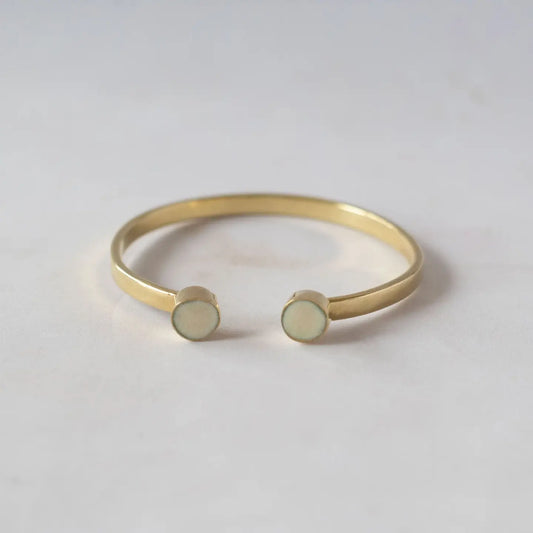 Gold bracelet with two round, light-colored stones on a light gray background