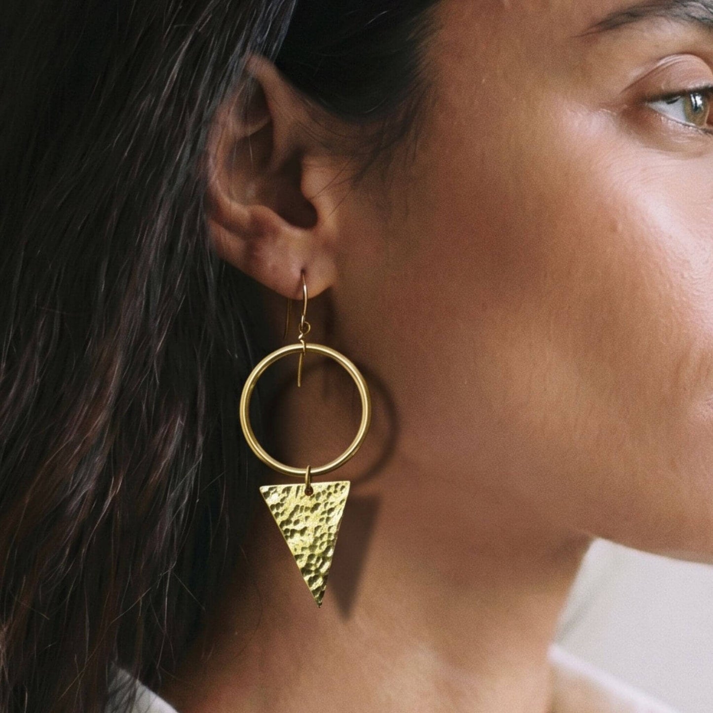 Close-up of a person wearing a gold hoop earring with a textured triangle detail.