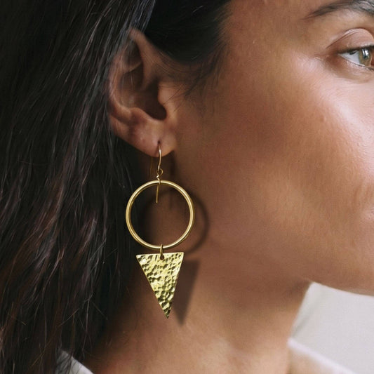 Close-up of a person wearing a gold hoop earring with a textured triangle detail.