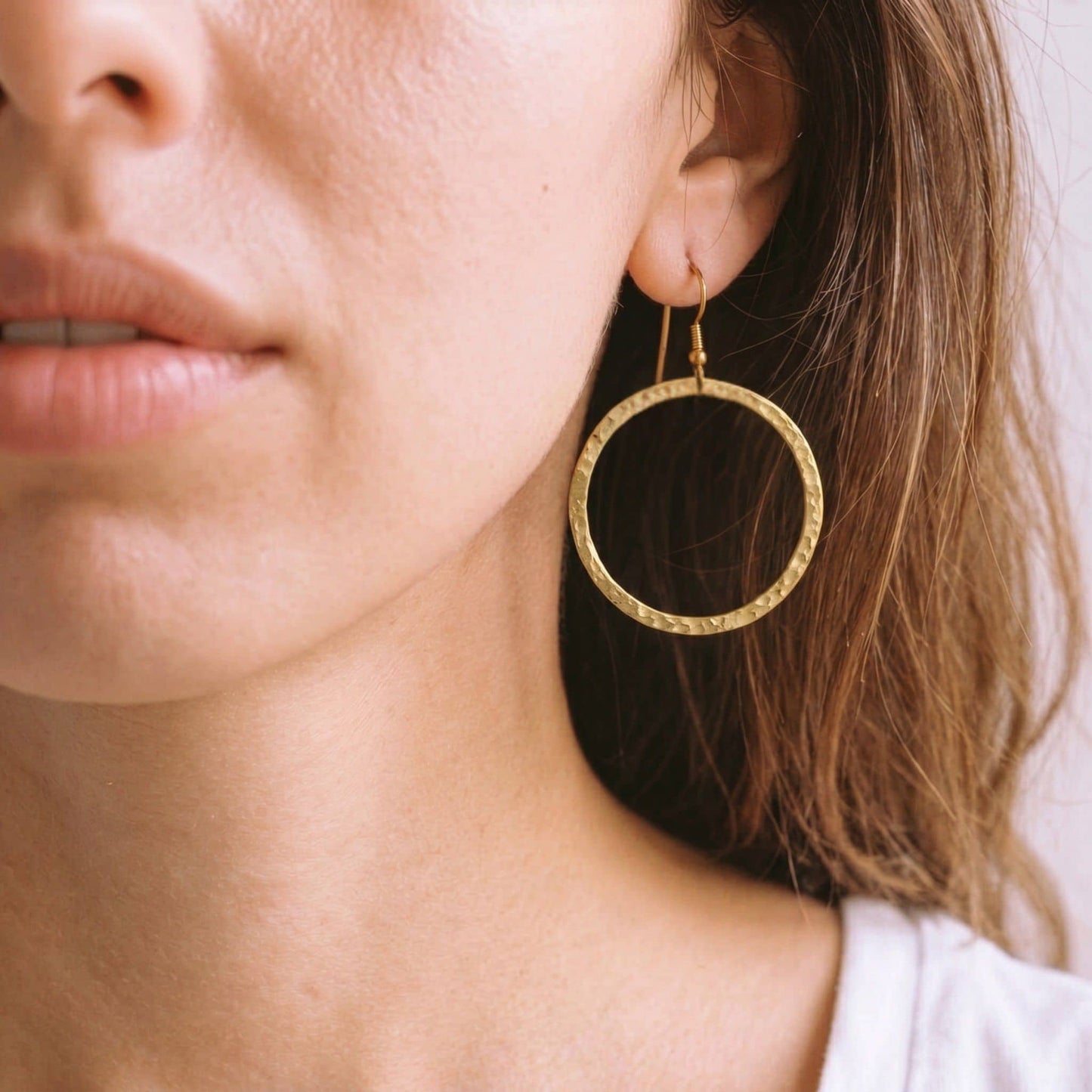 Close-up of a person wearing a gold circle hoop earring with a French hook.