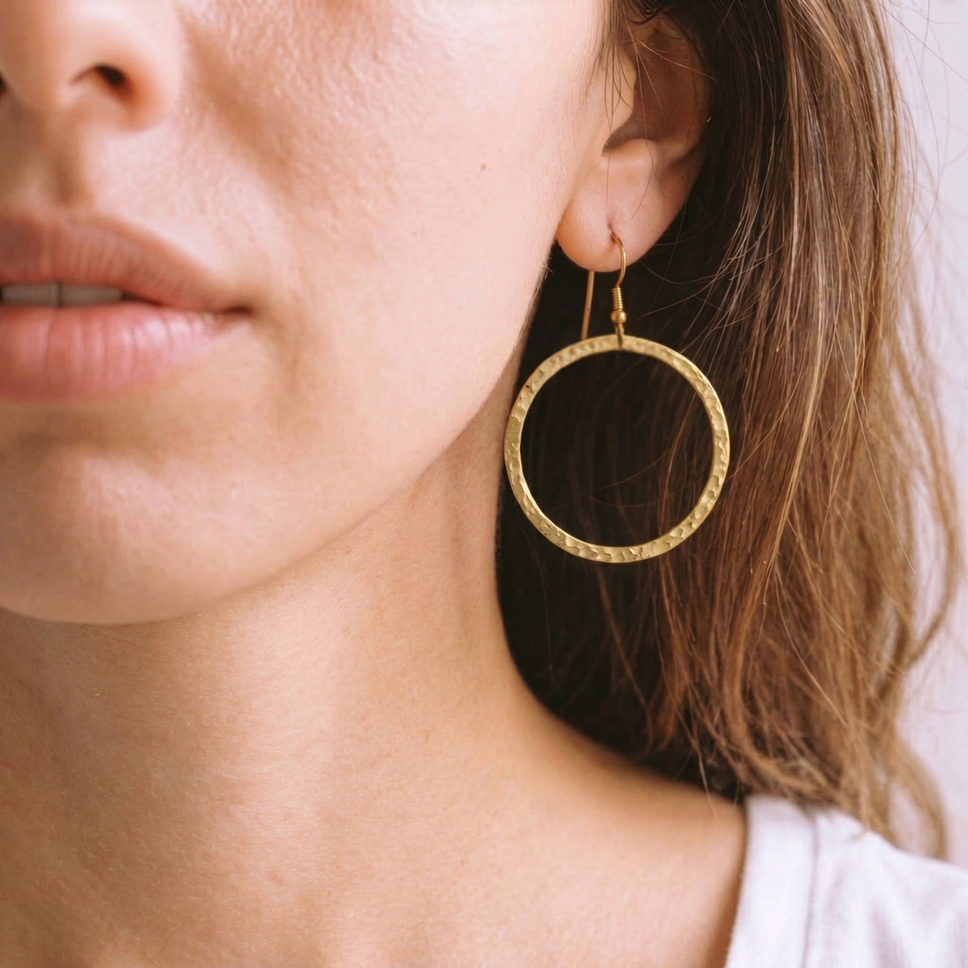 Close-up of a person wearing a gold circle hoop earring with a French hook.