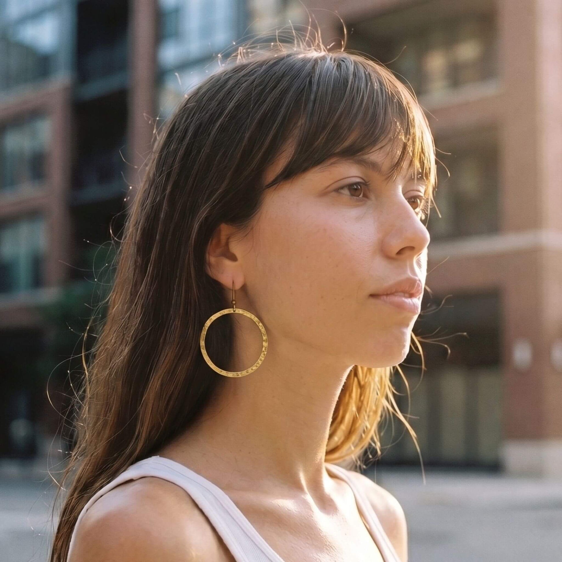 Woman wearing gold hoop earrings with a blurred urban background