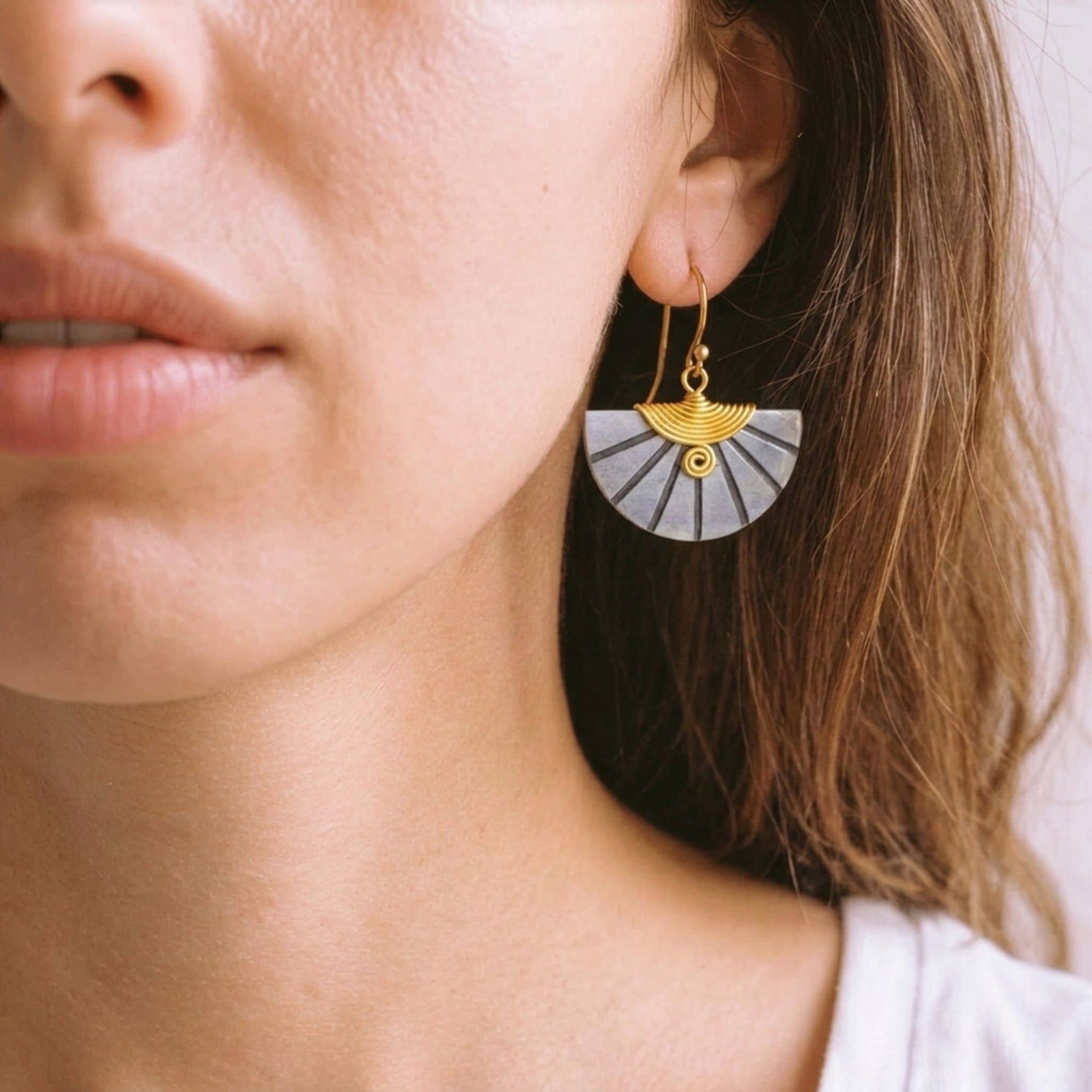 Close-up of a woman wearing gold and grey fan-shaped earrings.