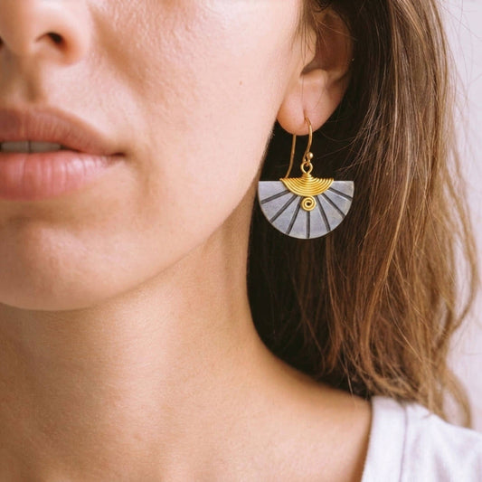 Close-up of a woman wearing gold and grey fan-shaped earrings.