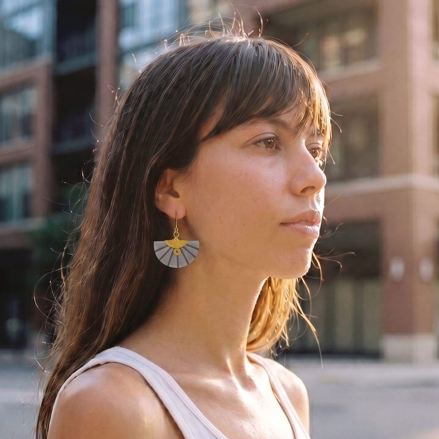 Woman wearing a unique grey and gold fan-shaped earring in an urban setting