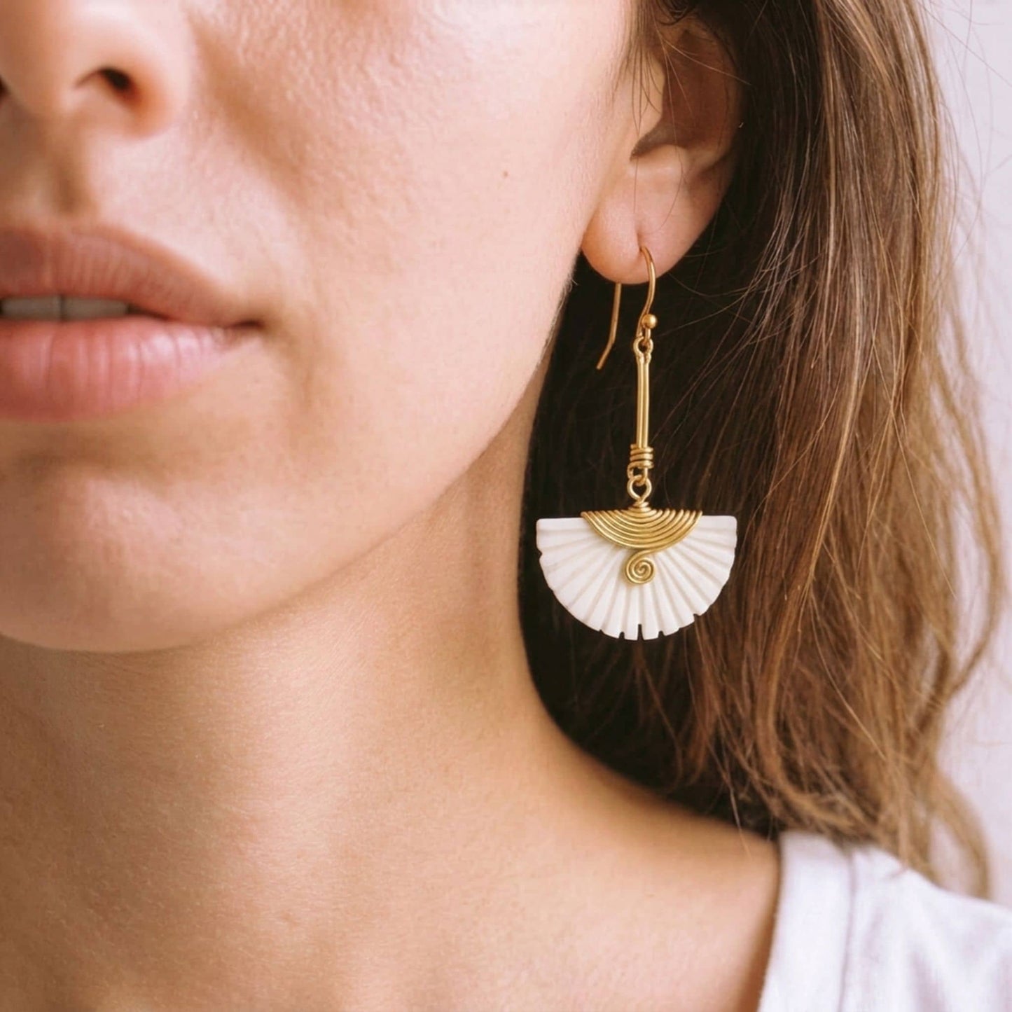 Close-up of a woman wearing gold-tone and white bone earrings.