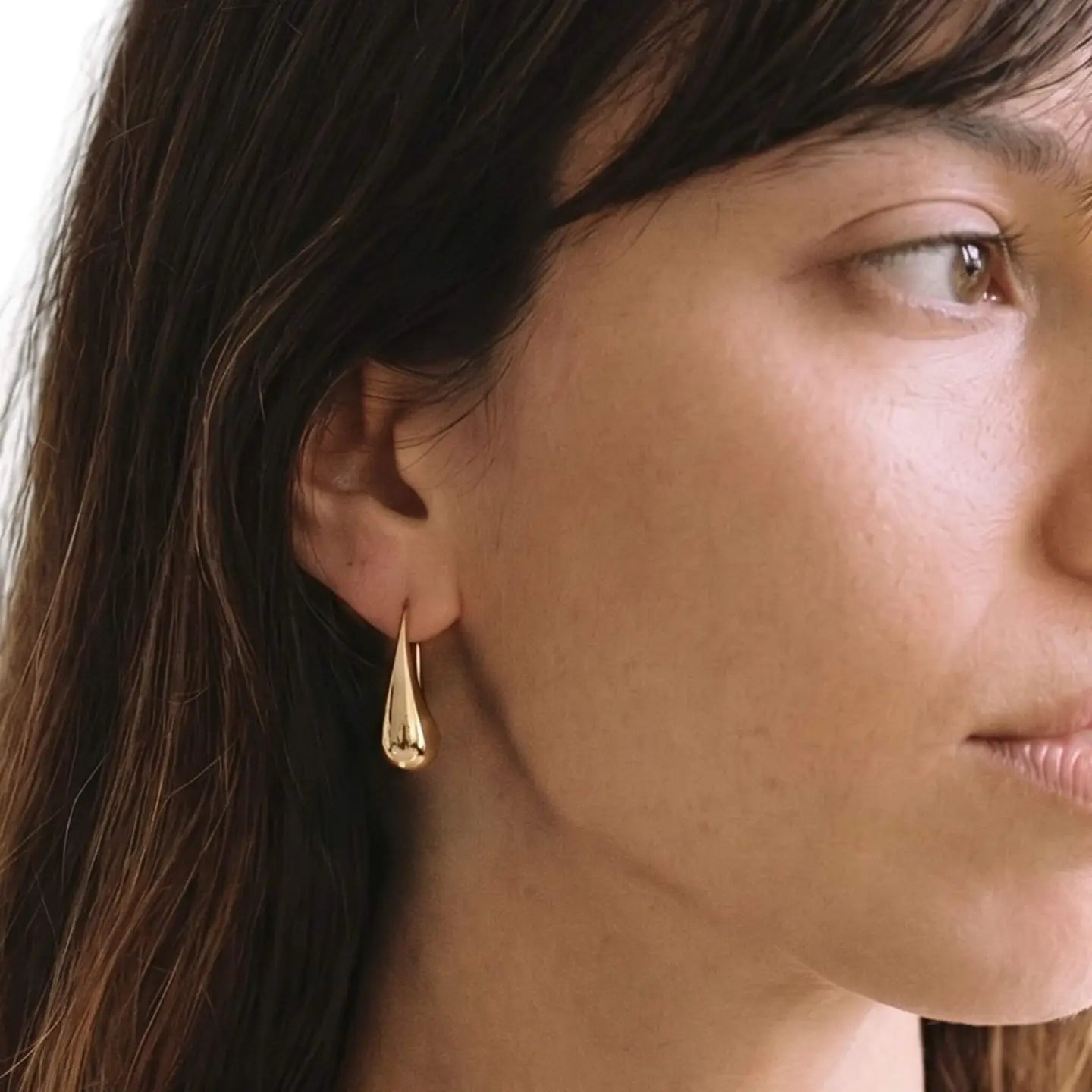 Close-up of a woman wearing a gold teardrop earring with a neutral background