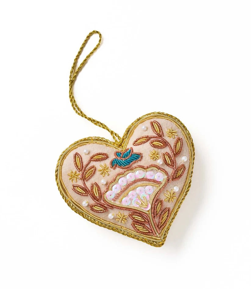 Heart-shaped ornament featuring cream and brown beadwork, colorful floral details and a bright blue bird at the center.