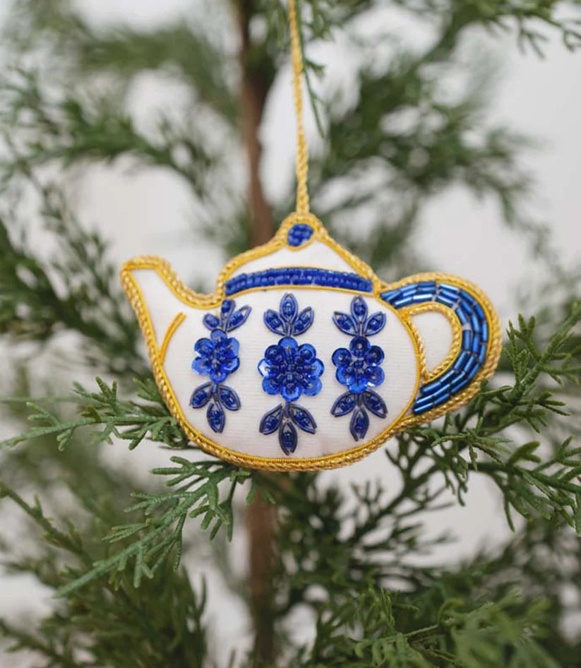 Close-up of a handcrafted teapot ornament showing intricate blue floral details, beads and embroidered accents.