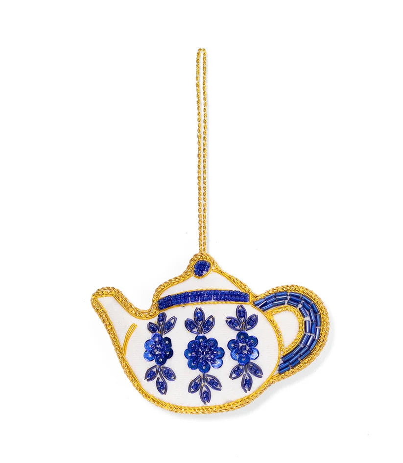 Creamy white teapot ornament featuring blue floral embroidery, detailed beadwork and a metallic gold hanging cord.