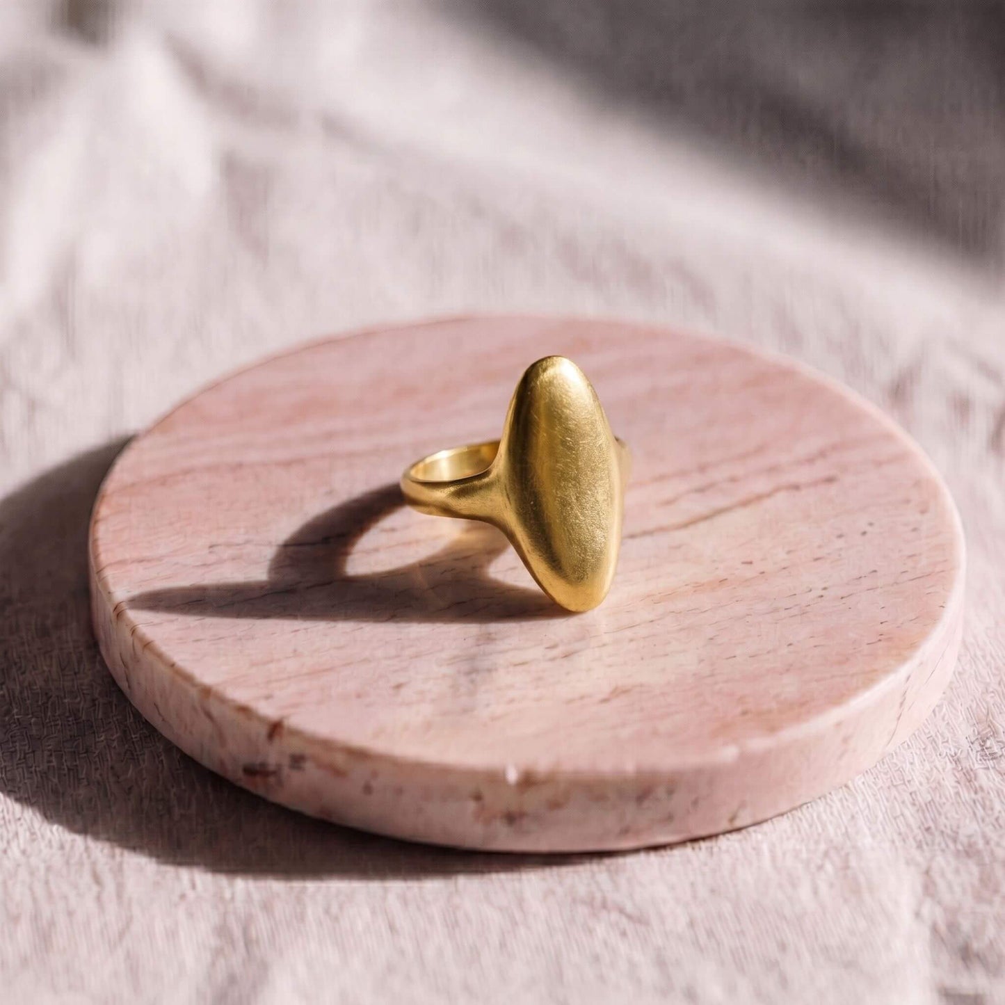 Gold ring on a pink marble coaster with a soft background
