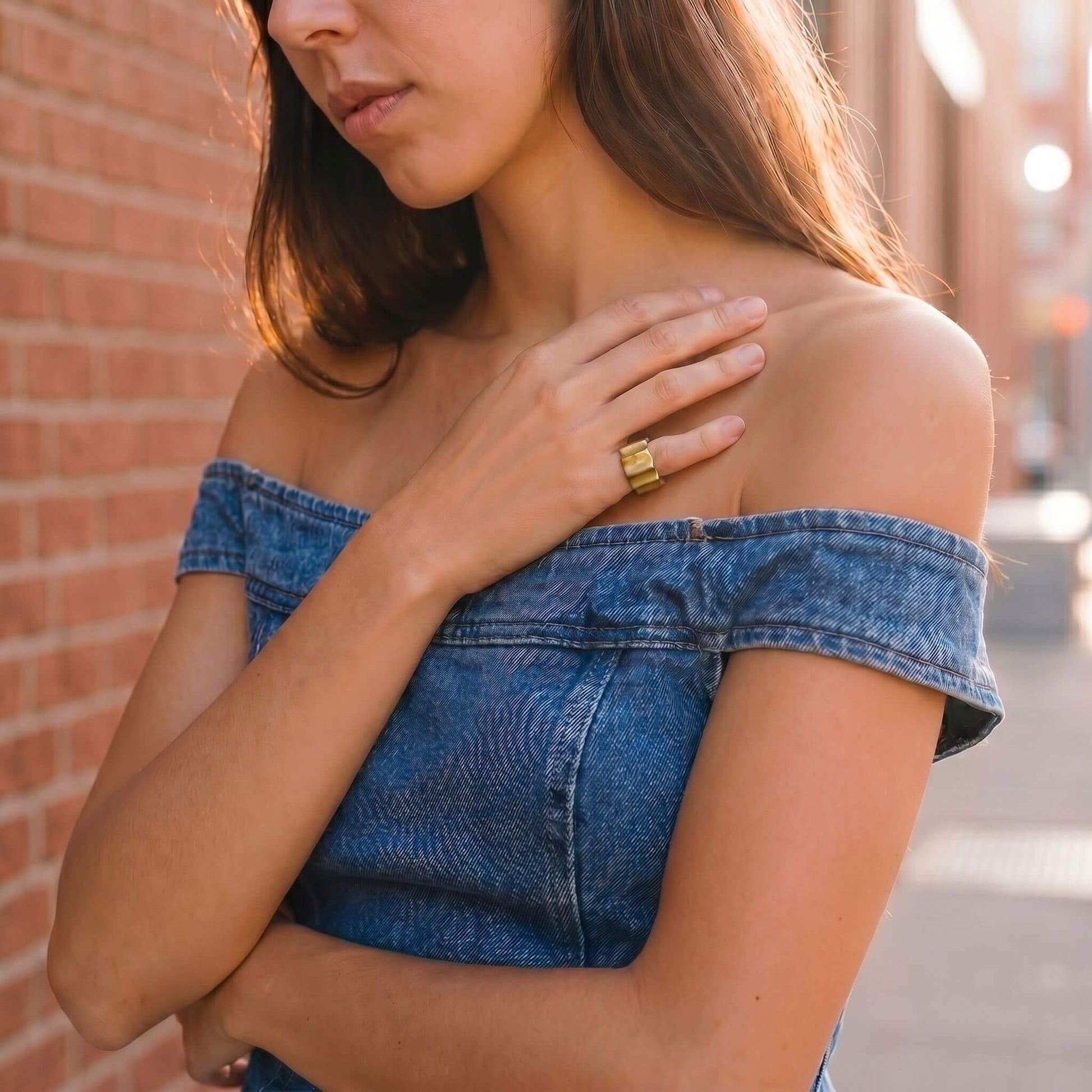 Woman wearing a blue denim off-shoulder top against a brick wall.