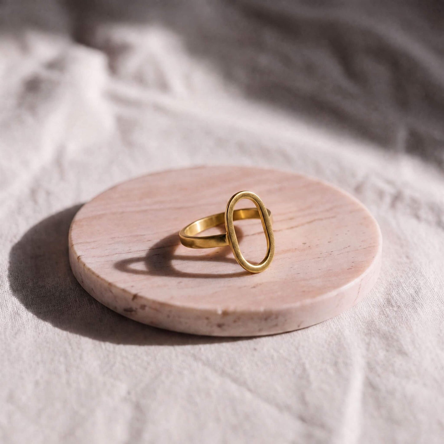Gold ring on a round wooden platform with a soft white background