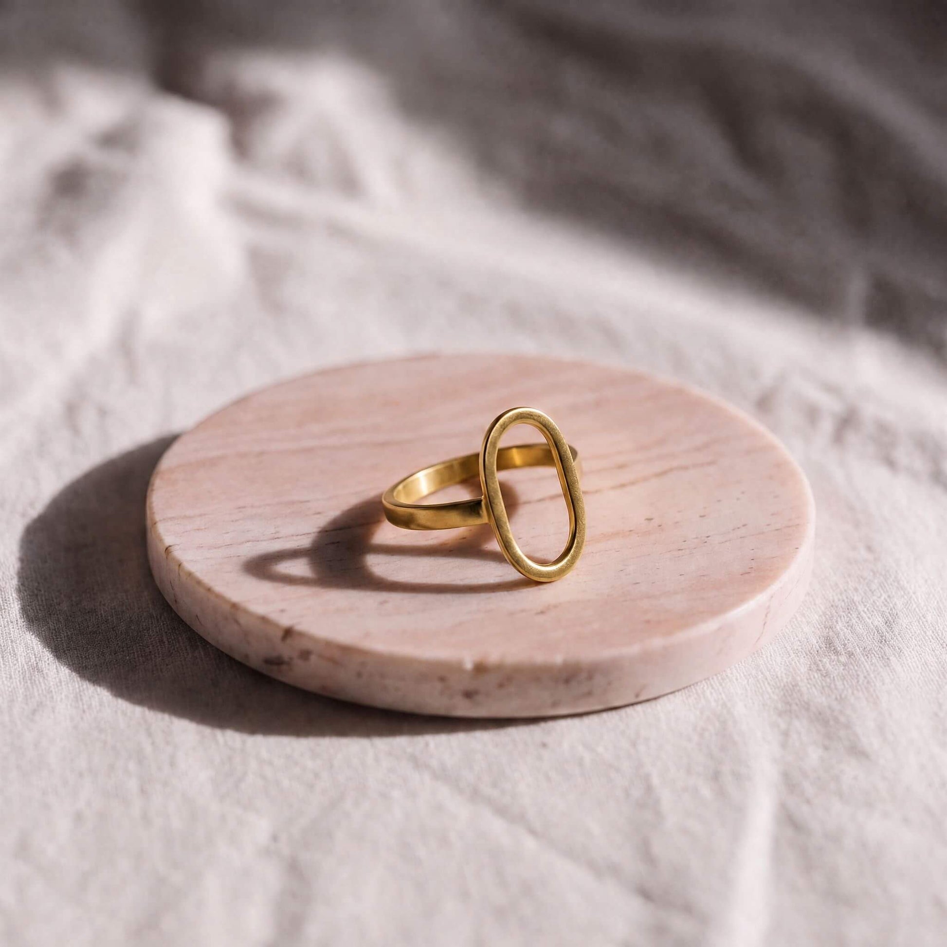 Gold ring on a round wooden platform with a soft white background