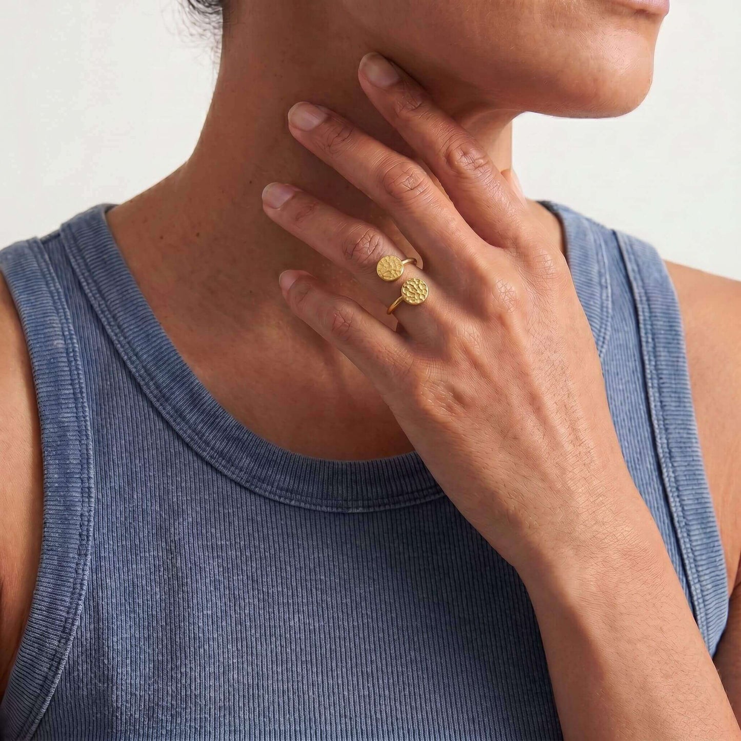Woman wearing a gold ring on her finger, touching her neck with a neutral background