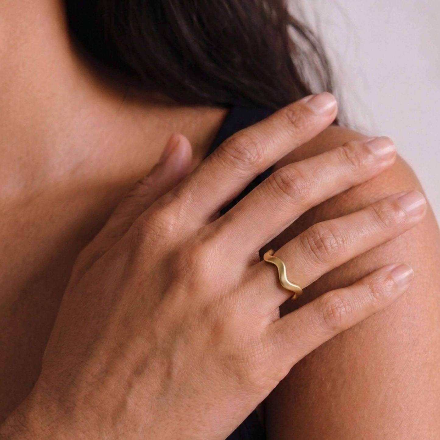 Close-up of a hand wearing a gold ring with a wavy design