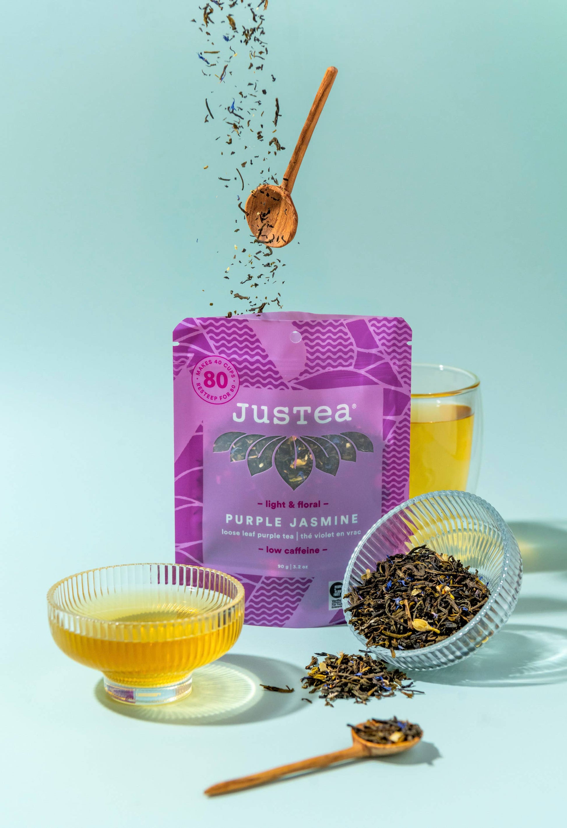 Justea Purple Jasmine tea packaging with a glass of tea and tea leaves on a light blue background