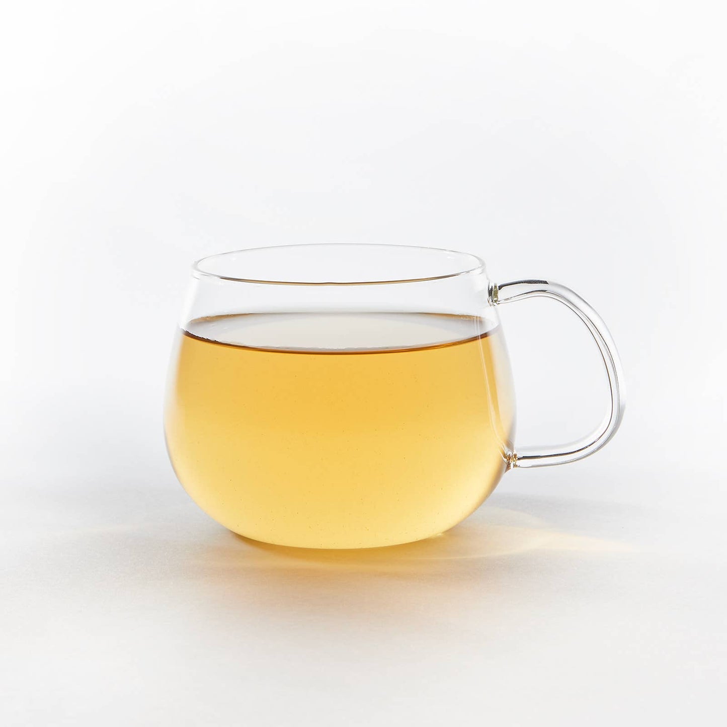 Clear glass mug with handle filled with yellow liquid on a white background