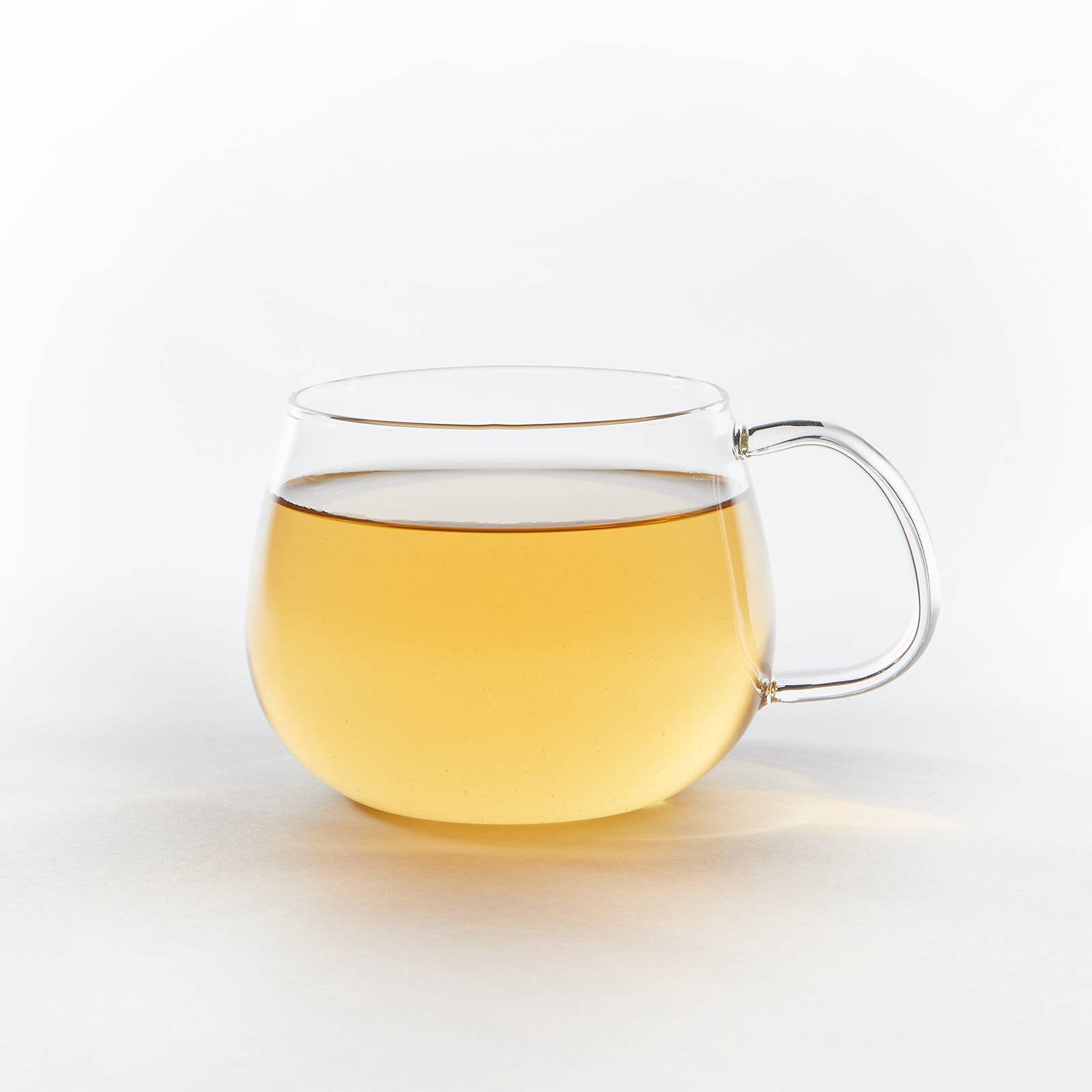 Clear glass mug with handle filled with yellow liquid on a white background
