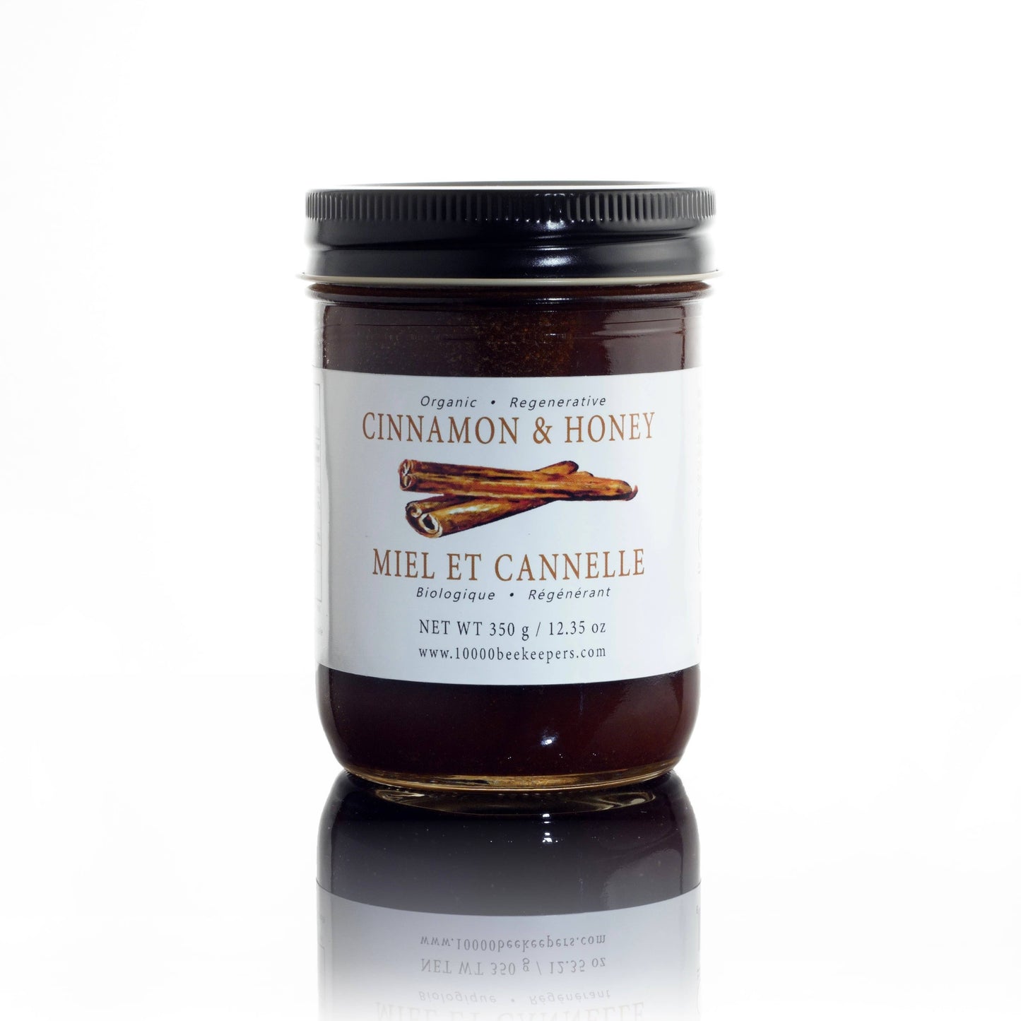 Jar of cinnamon honey spread with a white label on a reflective surface.