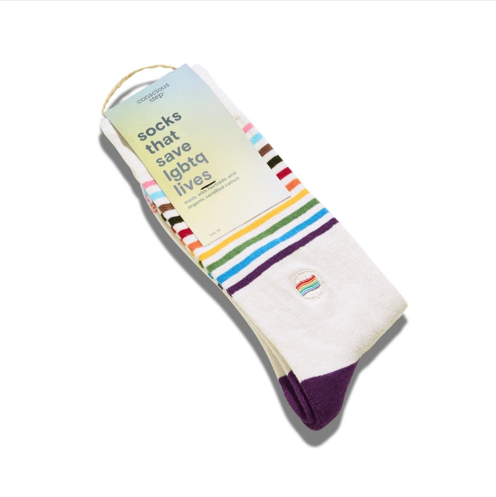 A pair of white socks with rainbow stripes and a purple toe, packaged with a paper tag that reads 'socks that save LGBTQ+ lives' on a white background.