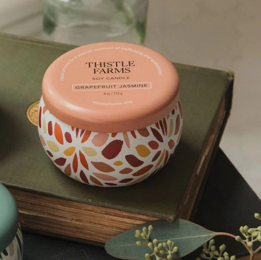 Thistle Farms soy candle with grapefruit jasmine scent on a book