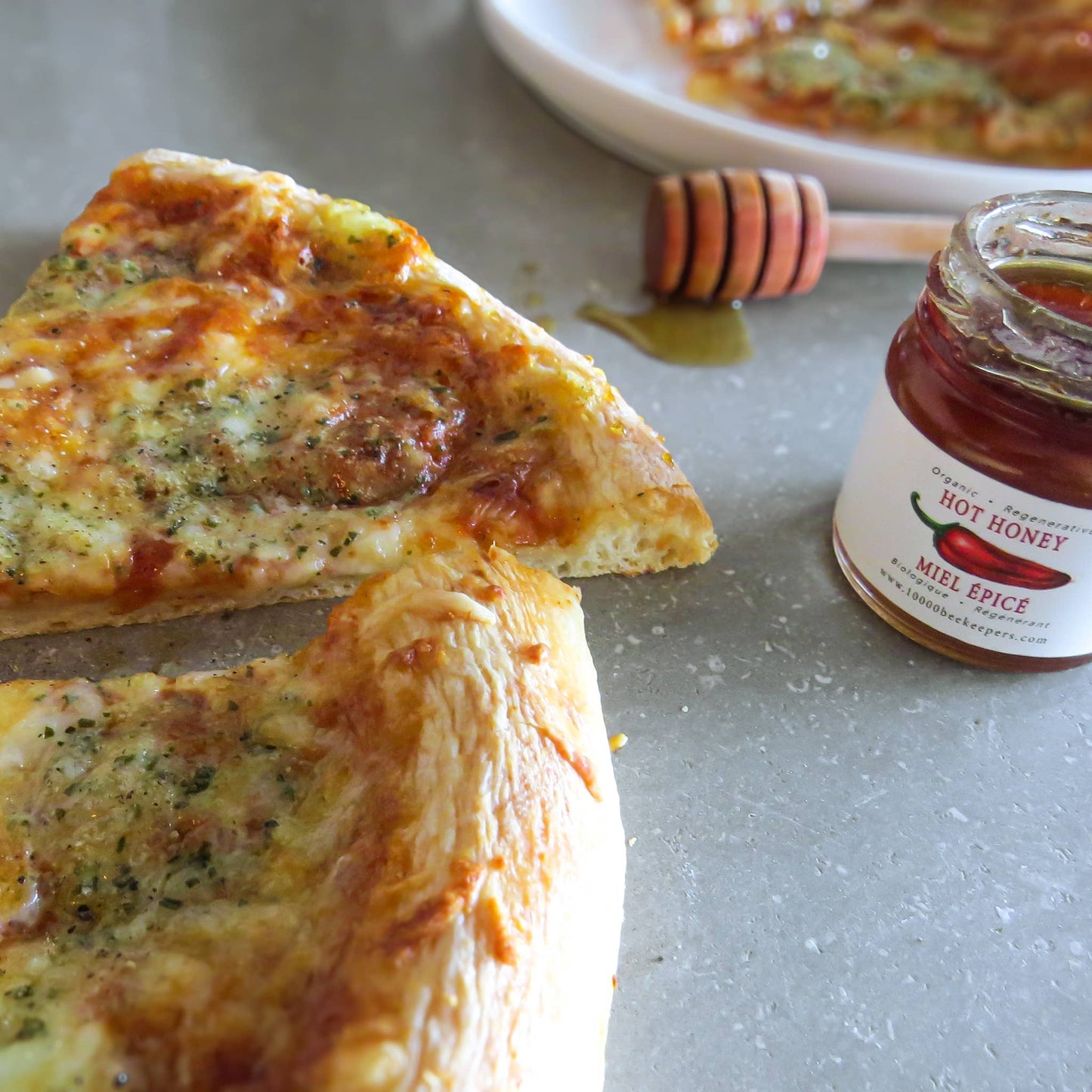 Two slices of pizza with a jar of hot honey on a gray table.