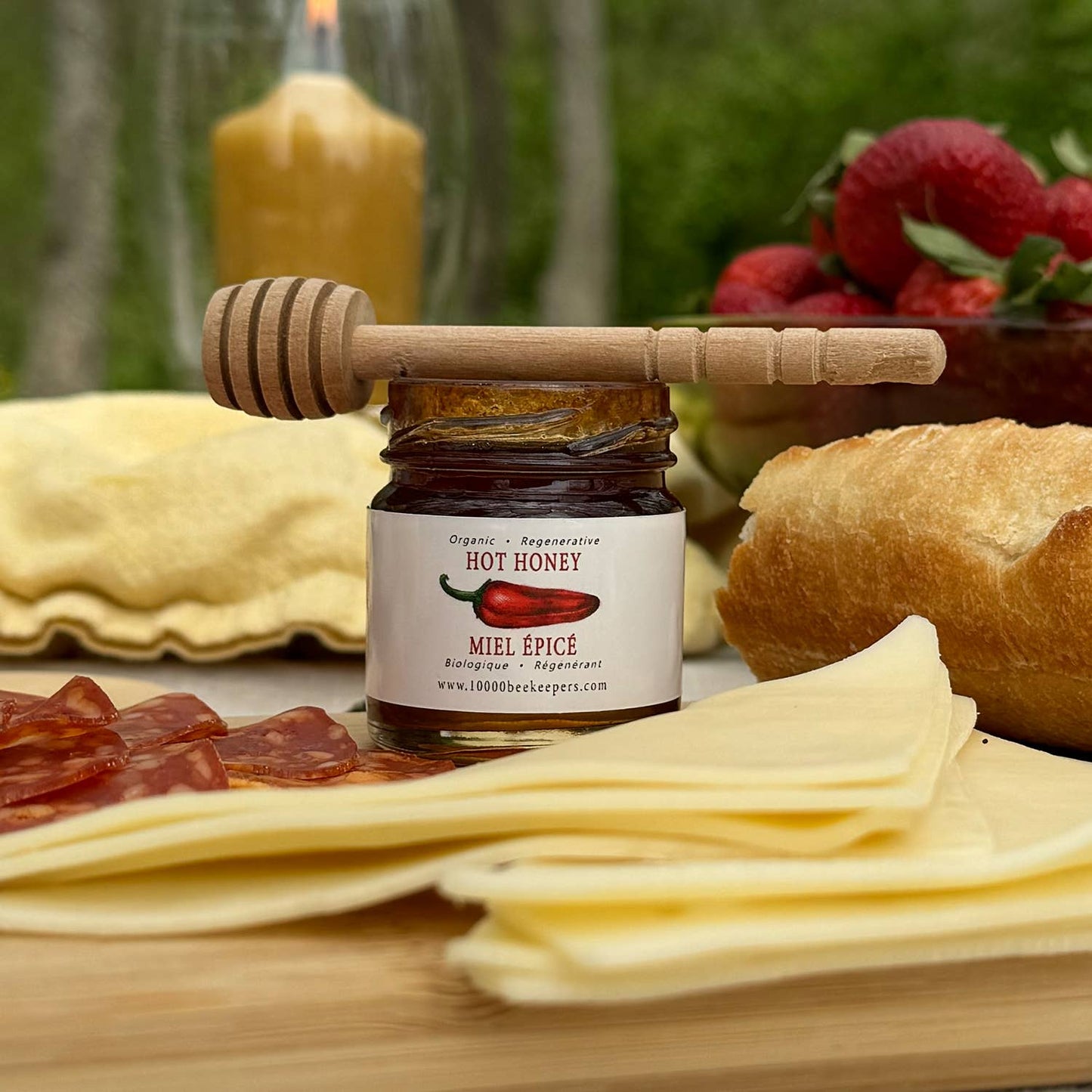 Jar of hot honey with a wooden dipper on a wooden board with cheese, salami, and bread.
