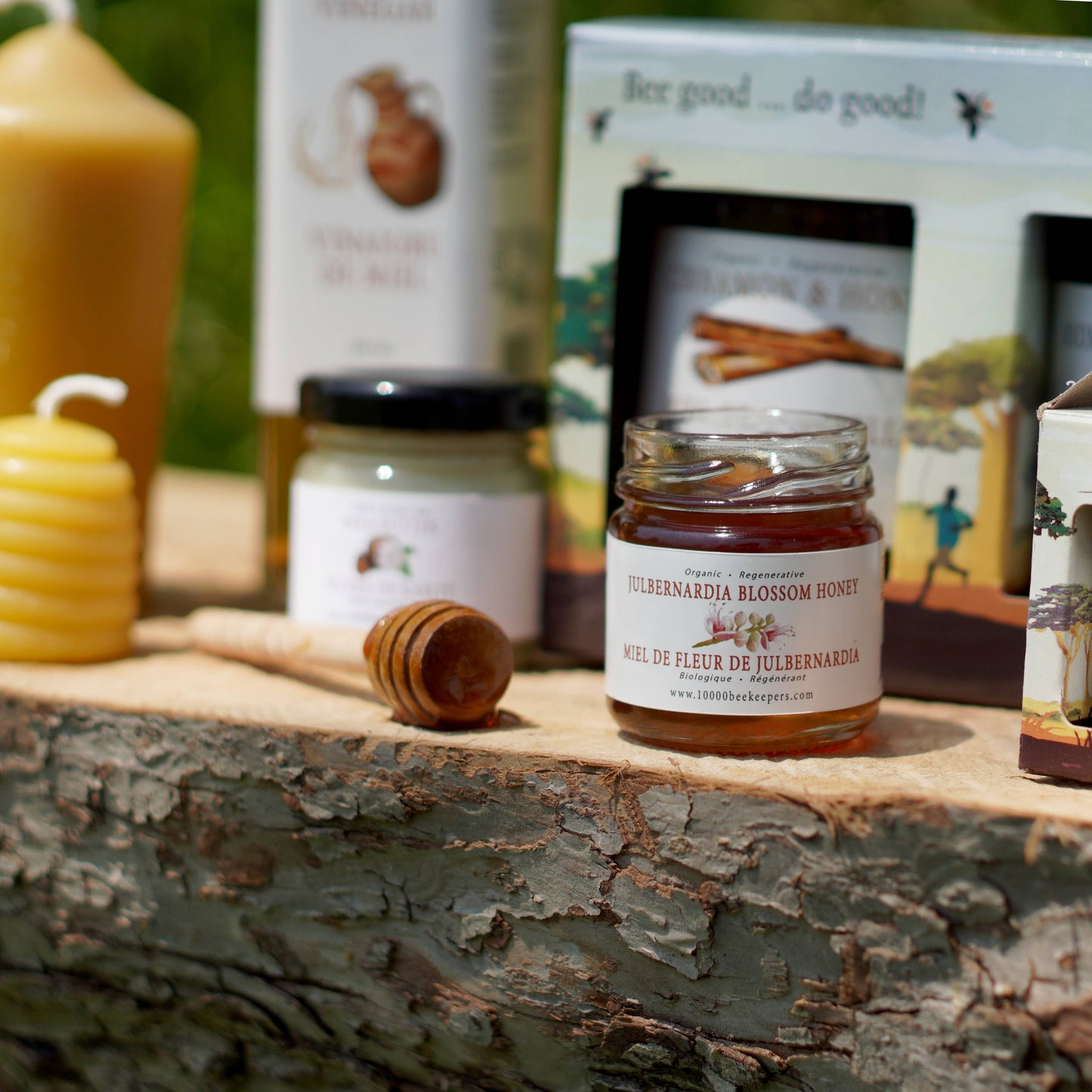 Jar of honey on a wooden surface with a background of other honey products and beeswax candles.
