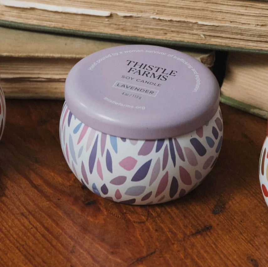 A purple candle tin is on a dark wooden table and surrounded by vintage books.